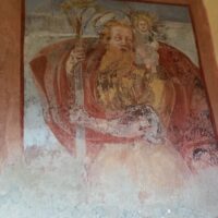 Il santo, con largo mantello e palma, guarda il Bambino, vestito di bianco con in mano un globo sormontato da una croce.